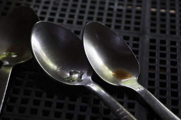 Polished metal spoons stand ready for use dark gridded surface. Reflective surfaces catch subtle...