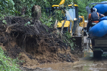 Heavy equipment clears massive landslide blocking muddy forest road. Urgent efforts restore...