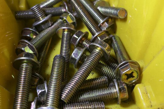 Large pile of industrial metal hardware. Many shiny yellow steel bolts and screws fill container. These fasteners are for construction, maintenance, and repair projects