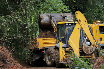 Yellow backhoe loader clearing mud and soil with bucket on rural road. Powerful construction...