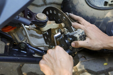Close up of focused mechanic with dirty hand doing repair service. Man performing vehicle maintenance on quad bike brake disc, caliper, and suspension © CoreRock