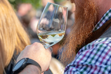 A man with a red beard holds a glass of white wine at a wine festival in Retz.