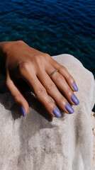 A macro close-up of a pale woman's hand with violet nail polish resting on a light fabric. Elegant minimalism captured in natural seaside light.