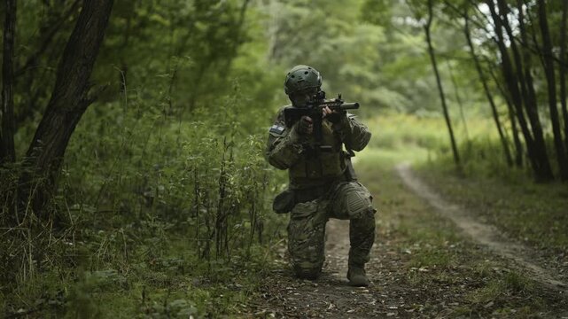 Camouflaged and masked army soldier with AR15 carbine on a mission. Carefully sneaking through a thick green forest then pausing to take aim with a collimator