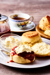 紅茶とともに楽しむアフタヌーンティーのスコーン。クロテッドクリームとジャムを添えて味わう伝統的な英国風ティータイムの一場面。ティーポットやカップと共に並べられたスコーンは、洋菓子、デザート、カフェ、休日のひとときを表現する素材写真として利用可能。