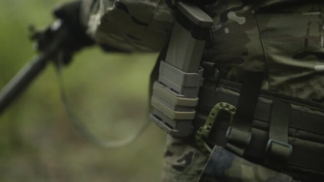 Camouflaged and masked army soldier with AR15 carbine on a mission. Close-up on the rifle