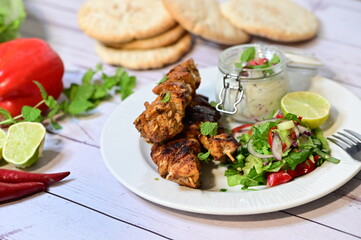 Chicken kebab served with raita and fresh salad on a white plate, light background, healthy and delicious popular meal.