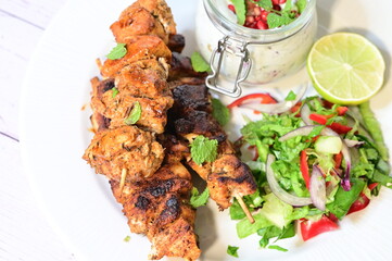 Chicken kebab served with raita and fresh salad on a white plate, light background, healthy and delicious popular meal.
