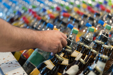 Hand selecting a beverage from a colorful display of various soda and beer bottles in a market setting