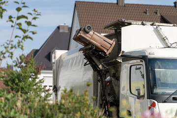 Obraz premium Garbage truck collecting brown bin on a sunny day in suburban neighborhood with houses in the background