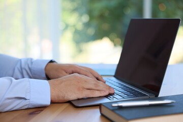 Man working on laptop at wooden table indoors, closeup