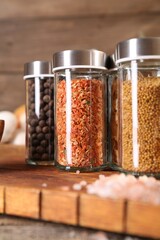 Different spices in glass jars and on wooden table, closeup
