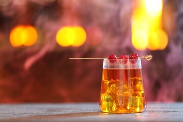 Glass of alcoholic cocktail with garnish on table against blurred background with smoke, space for text. Bokeh effect