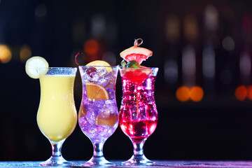 Glasses of alcoholic cocktails with garnish on table against blurred background, space for text