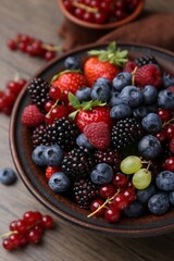 Different ripe berries in bowl on wooden table, closeup