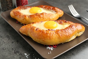 Tasty khachapuris with cheese and eggs served on grey table, closeup
