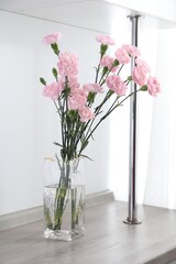 Beautiful carnation flowers in glass vase on wooden table indoors