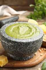 Tasty green pesto in mortar and ingredients on wooden table, closeup