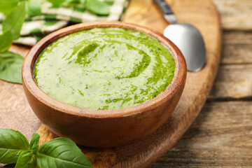 Tasty green pesto in bowl and basil leaves on wooden table, closeup