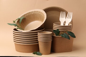 Set of disposable tableware and green leaves on dark beige background, closeup
