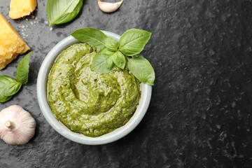 Fresh pesto sauce and ingredients on black textured table, flat lay. Space for text