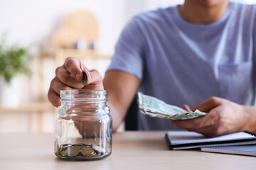 Man putting money into jar at wooden table indoors, closeup