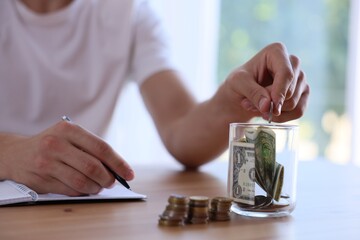 Man putting money into jar at wooden table indoors, closeup