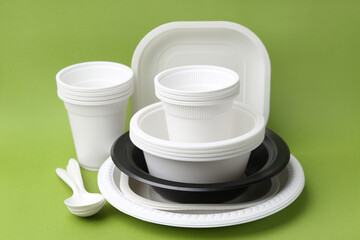 Set of disposable plastic tableware on light green background, closeup