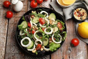 Delicious squid salad and ingredients on wooden table, flat lay