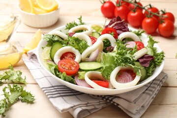 Delicious salad with squid rings and vegetables on light wooden table, closeup