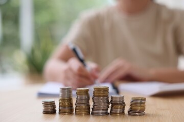 Woman working at wooden table indoors, focus on stacks of coins
