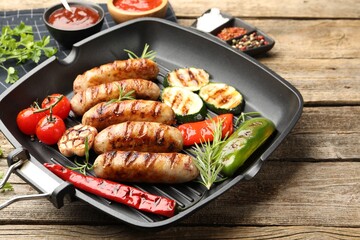 Pan with grilled sausages, vegetables, spices and sauces on wooden table, closeup