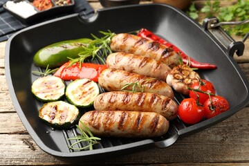 Pan with grilled sausages, vegetables and spices on wooden table, closeup