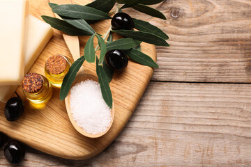Handmade soap bars, olives, green leaves, sea salt and essential oils on wooden table, top view. Space for text