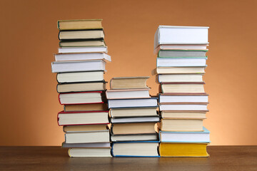 Stacks of many books on wooden table against light brown background