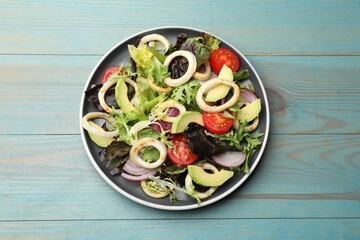 Delicious salad with squid rings, avocado and vegetables on light blue wooden table, top view