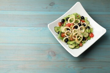 Delicious salad with squid rings, olives and vegetables on light blue wooden table, top view. Space for text