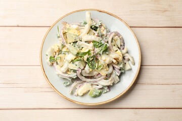 Tasty salad with squid rings, onion and eggs served on light wooden table, top view