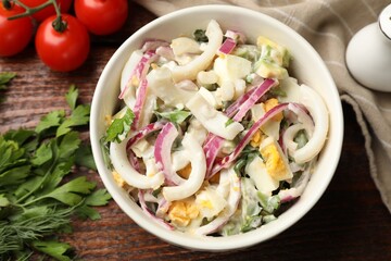 Tasty salad with squid rings, onion and eggs served on wooden table, flat lay