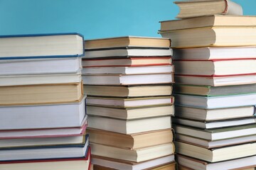 Many stacked books against light blue background, closeup