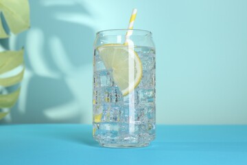 Refreshing water with lemon and ice on light blue background, closeup