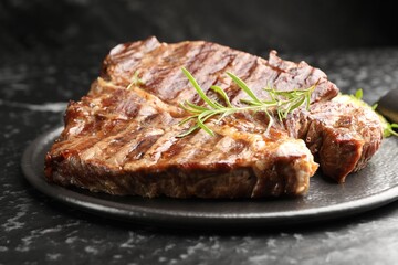 Delicious grilled beef steak with rosemary on dark textured table, closeup