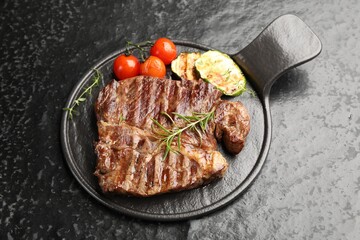 Delicious grilled beef steak with rosemary, zucchini and tomatoes on dark textured table