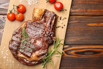 Delicious grilled beef steak with herbs, spices and tomatoes on wooden table, top view. Space for text