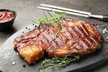 Delicious grilled beef steak with herbs, spices and ketchup on grey textured table, closeup