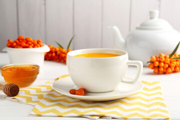 Sea buckthorn tea in cup, honey and fresh berries on white table, closeup