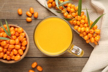Cup of sea buckthorn tea and fresh berries on wooden table, flat lay