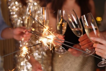 Friends celebrating New Year with sparklers and wine glasses indoors, closeup
