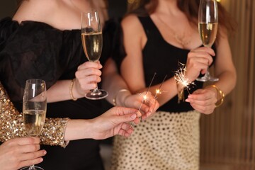 Women celebrating New Year with sparklers and wine glasses indoors, closeup