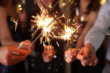 Friends celebrating New Year with sparklers and wine glasses indoors, closeup